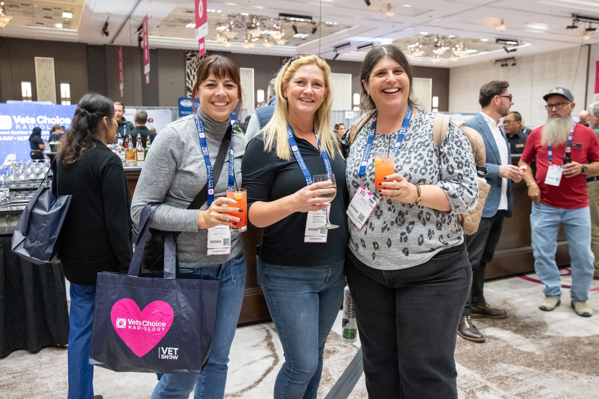 3 women smiling and enjoying drinks at the show floor mixer